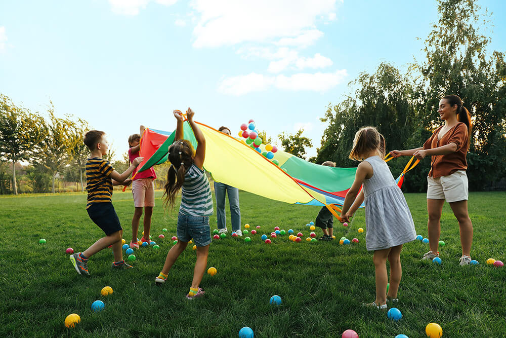 Kinder und eine Betreuerin halten Bälle auf einem großen Tuch in der Luft